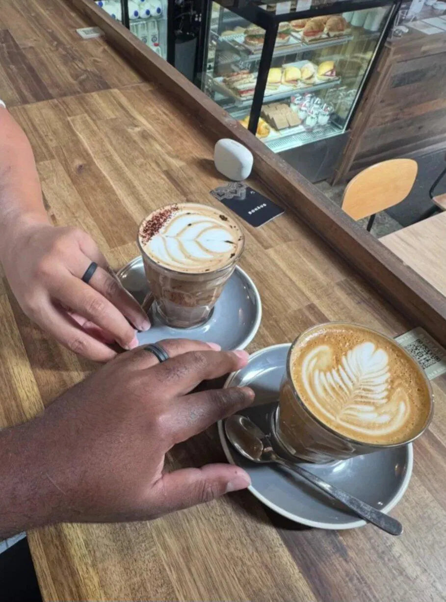Two hands resting by coffees on a café counter, each wearing a black silicone ring