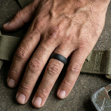 Hand wearing a black ring on a textured surface with green straps.