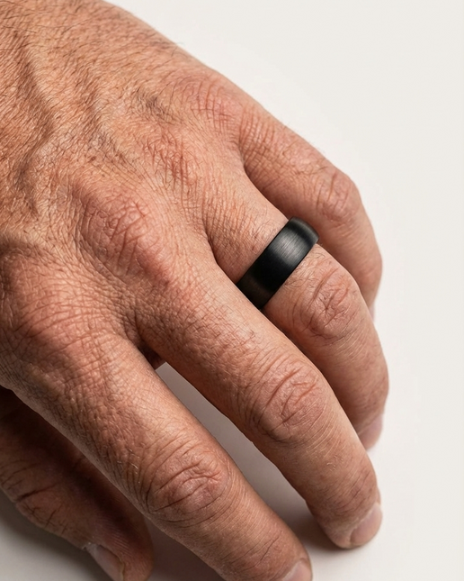 Hand wearing a black ring on a light background