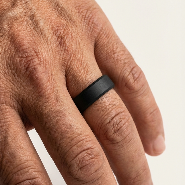 Close-up of a hand wearing a black ring on a light background