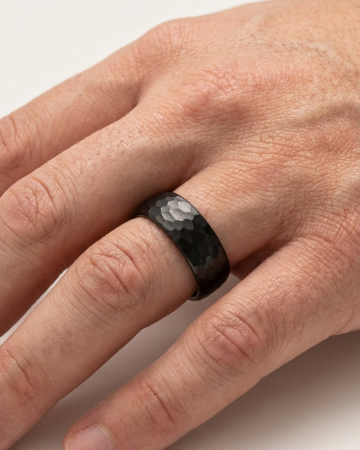 Hand wearing a black ring on a light background