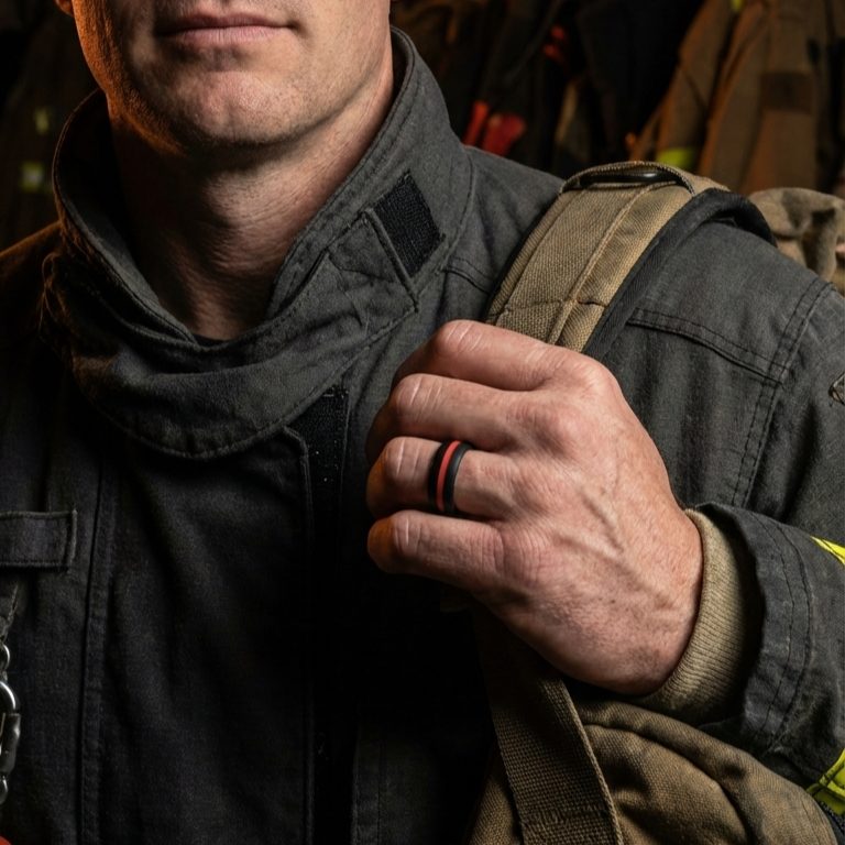 Firefighter in turnout gear holding a pack strap, wearing a black ring with a red stripe